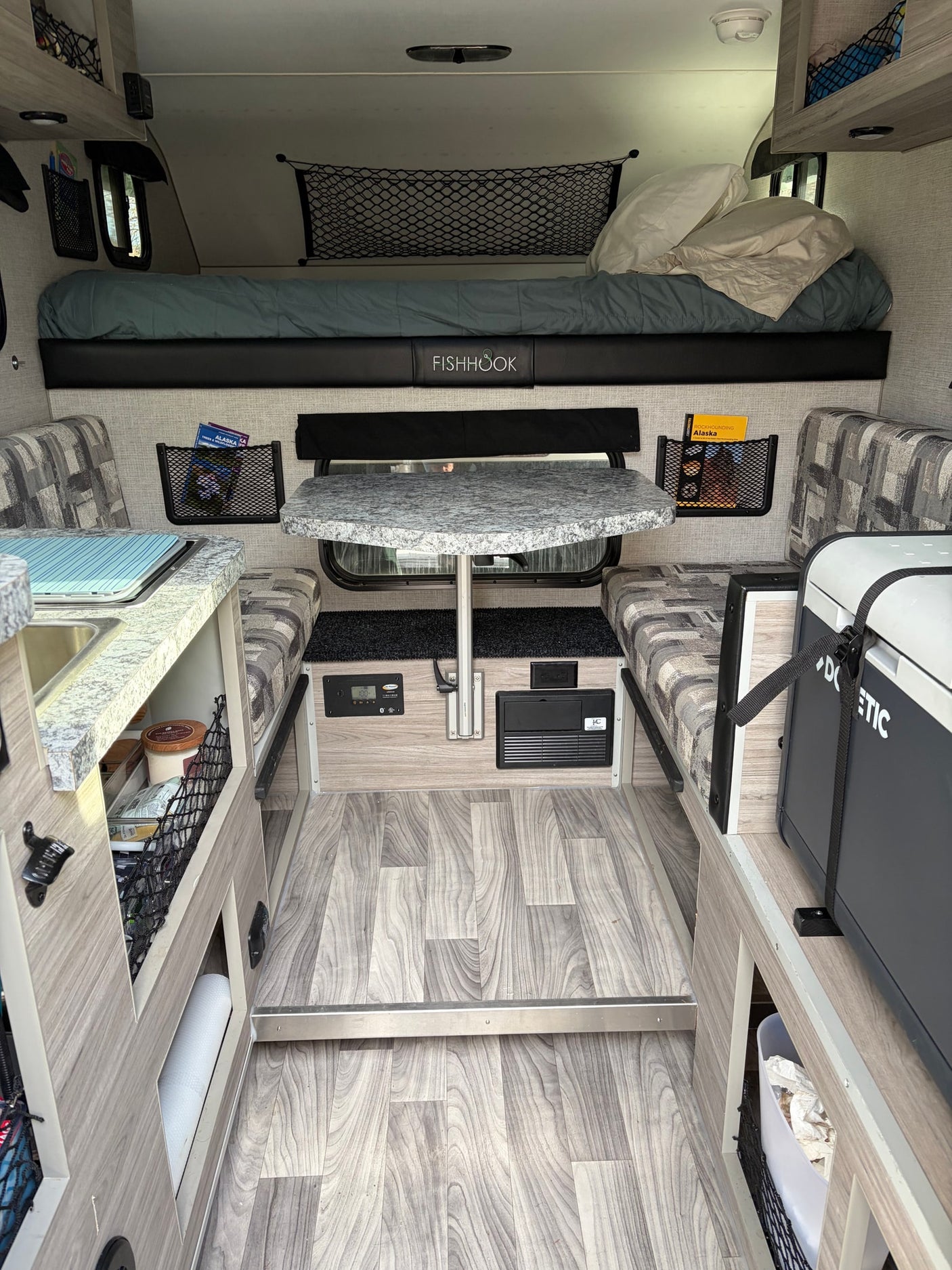 showing the interior of a Fishhook camper. Ideal for your rv rental trip.|Inside an RV rental through a screen door: view of the interior with a "FISHHOOK" bunk