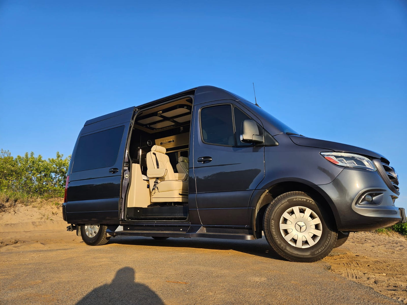 Spacious dark gray Sprinter van RV rental, side door open, revealing luxurious cream seating for comfortable travel.