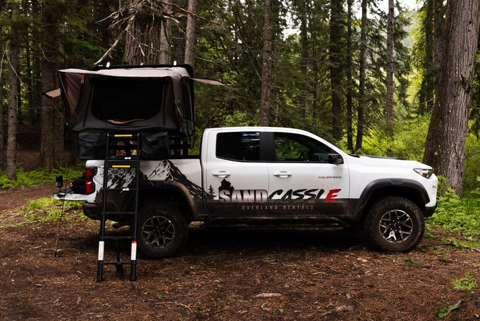 parked in a forest. Perfect RV rental for overlanding.|White pickup with rooftop tent & camp gear