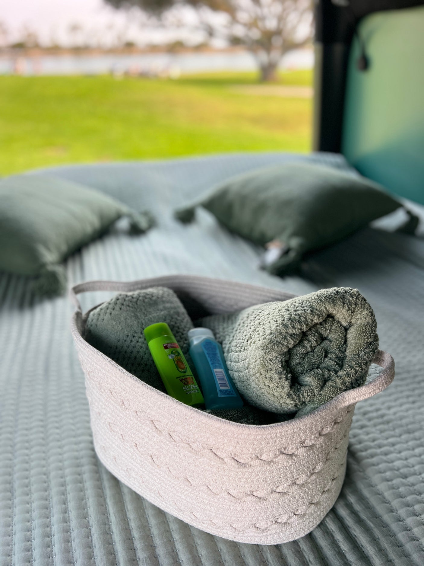 Inside an RV rental: A basket of fresh towels & toiletries rests on a quilted bed, offering comfort with a scenic view.