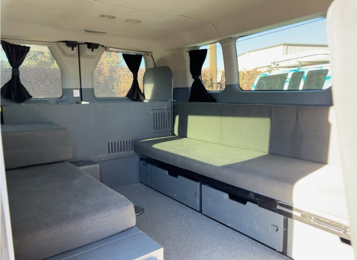 sliding door open to reveal interior swivel seat. Custom artistic wrap visible on side.|Inside an RV rental van: three black passenger seats