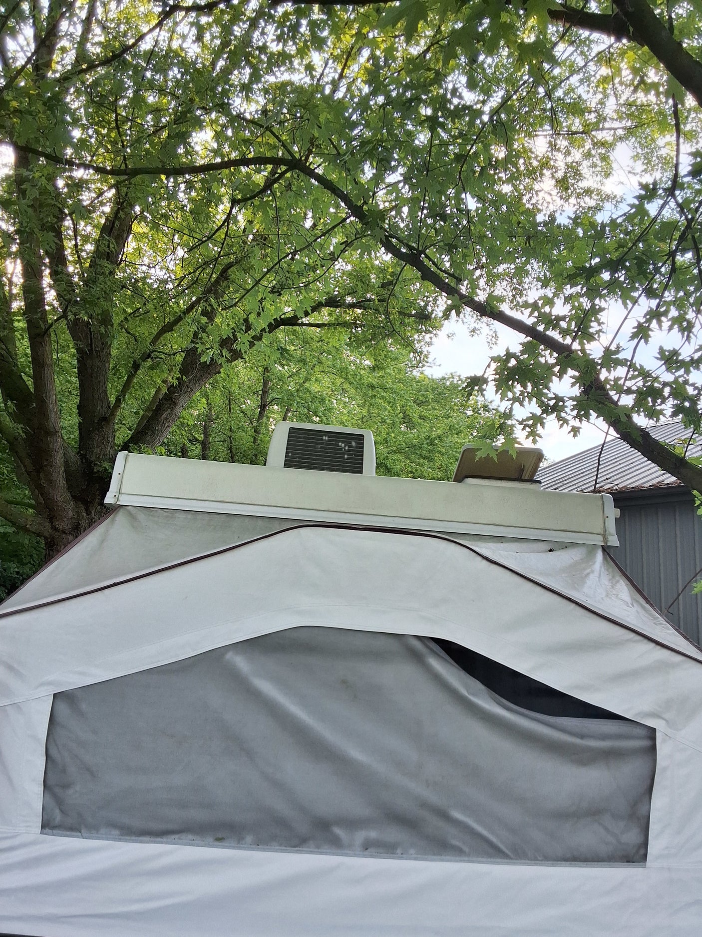 An rv rental pop-up camper's white canvas tent and roof AC unit are set amidst bright green trees, ready for camping.