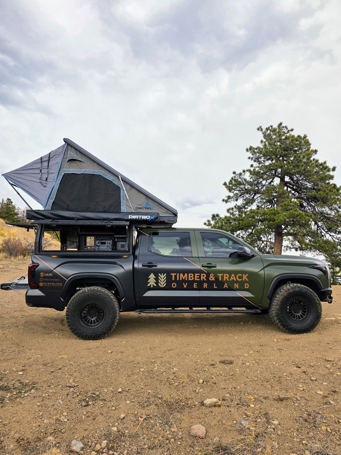 A green & black overland truck, branded 'Timber & Track Overland', with a rooftop tent. An ideal rv rental for off-grid camping.