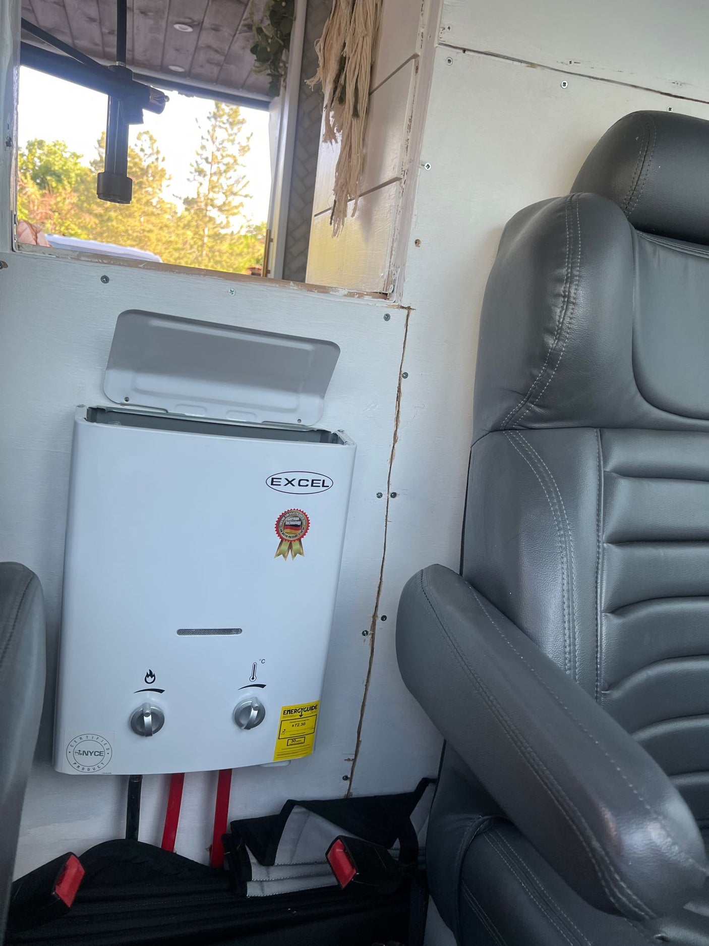 Inside an RV rental, a white Excel water heater is installed on the wall next to a comfortable grey passenger seat. Ideal for travel.