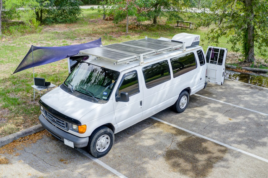 A white solar-powered camper van with awning and laptop setup, an ideal rv rental for mobile adventures.