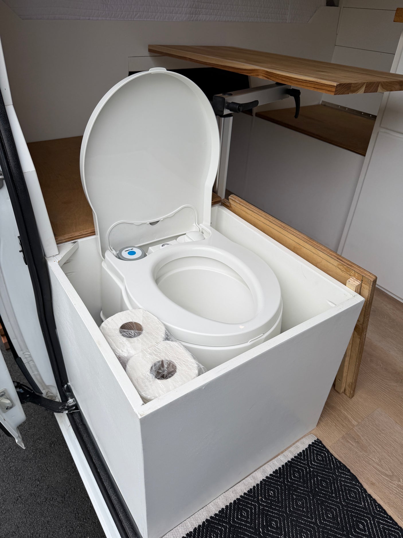 Essential for your RV rental: a clean Thetford portable toilet with lid open, neatly stored with toilet paper in a campervan.