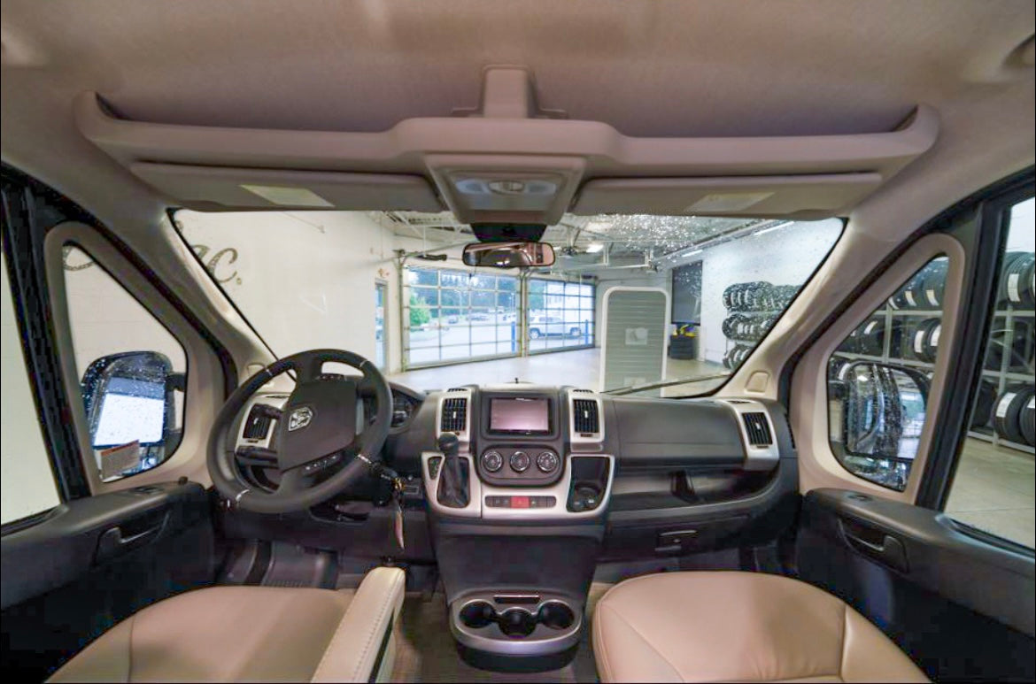 Front cabin of an RV rental van, showcasing its dashboard, steering wheel, and passenger seats.