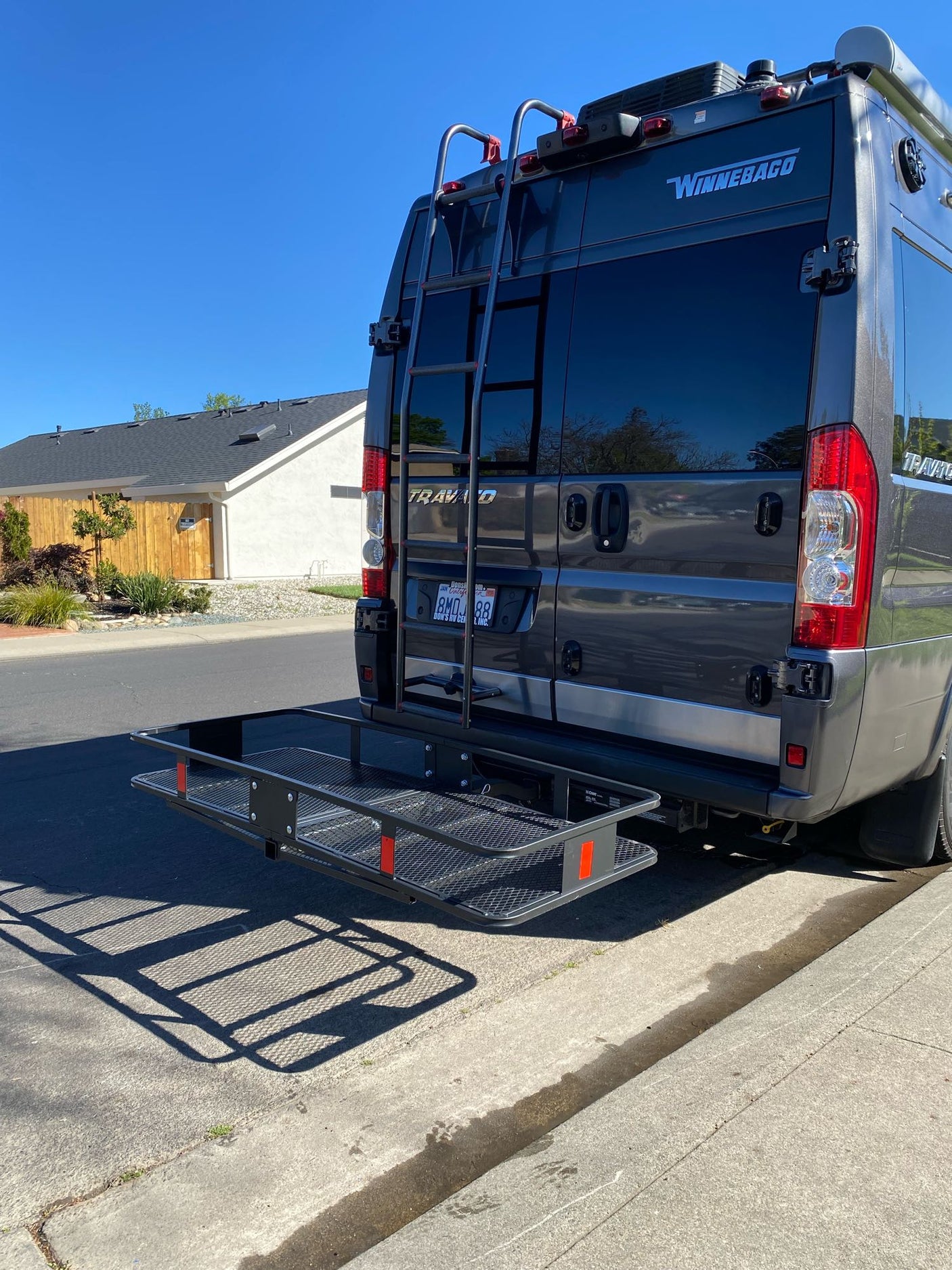 Gray Winnebago RV, equipped with a rear ladder and cargo carrier, perfect for an rv rental. Parked on a sunny street.