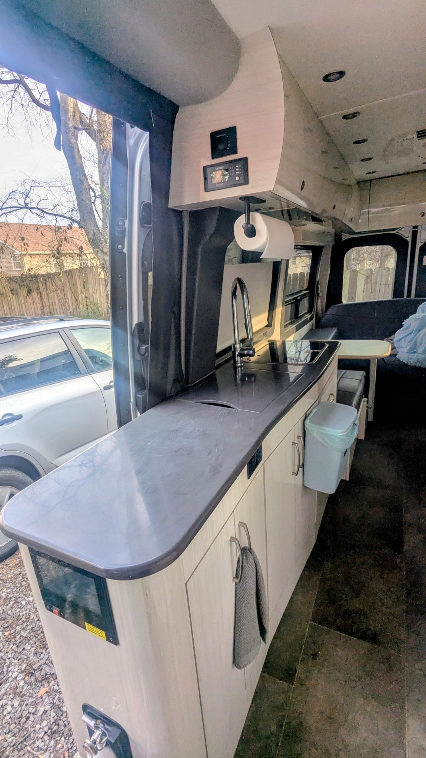 View inside an RV rental showing a compact kitchen area with a sink, faucet, counter, and overhead control panels.