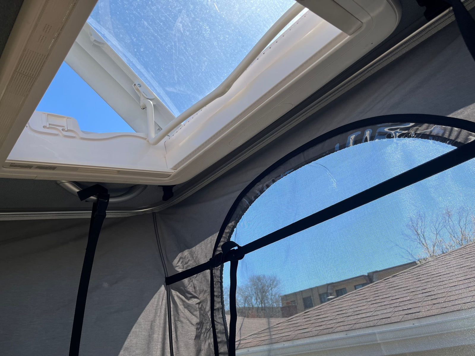 furry bed inside a cozy RV rental pop-top camper. Fabric walls and ceiling lights visible.|Cozy pop-top RV rental interior: elevated sleeping space with natural light and scenic views.|View from an RV rental: Bright blue sky seen through an open skylight and a mesh window