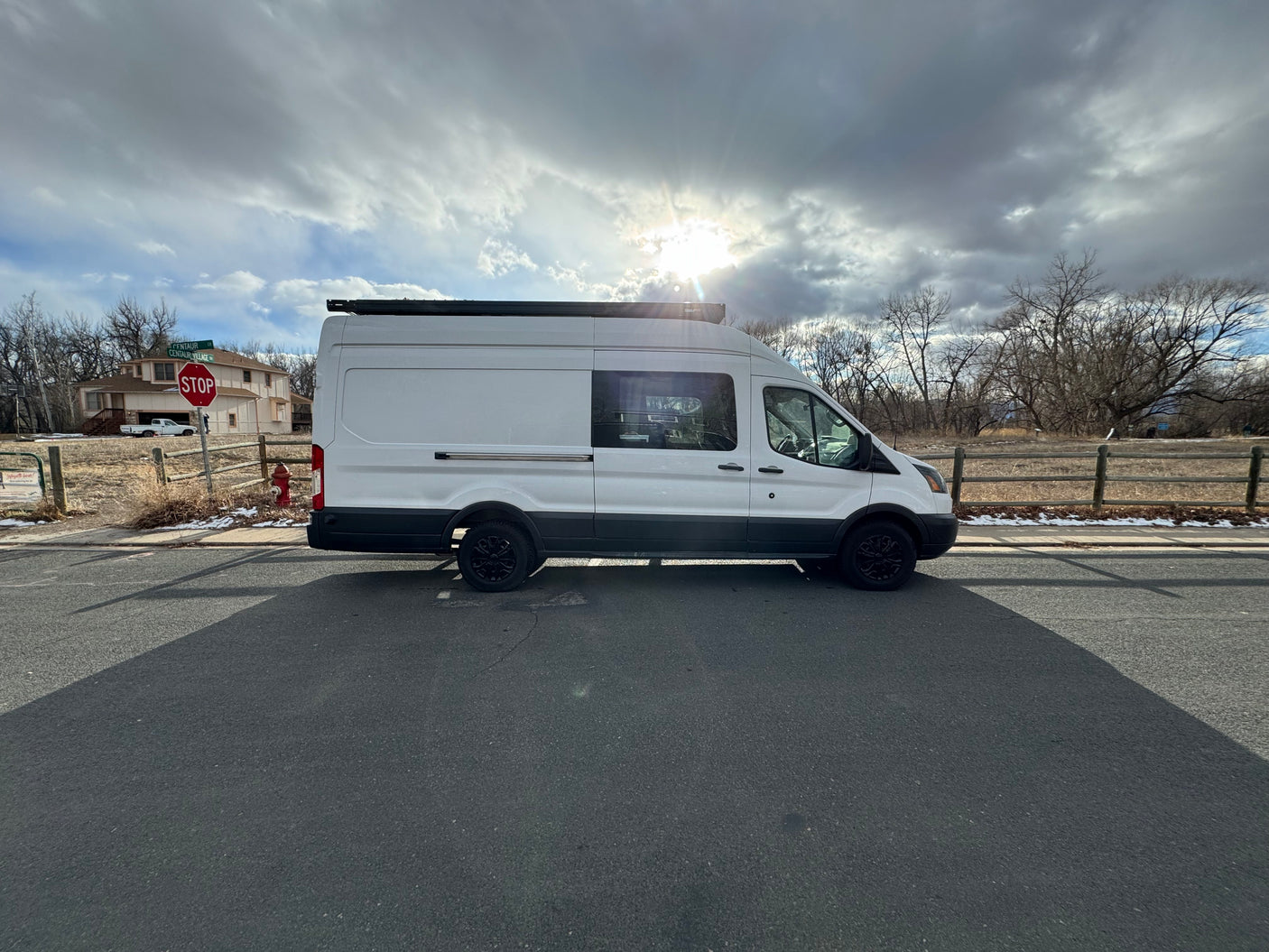 White camper van, resembling an RV rental, parked on a road under a sunlit, cloudy sky.