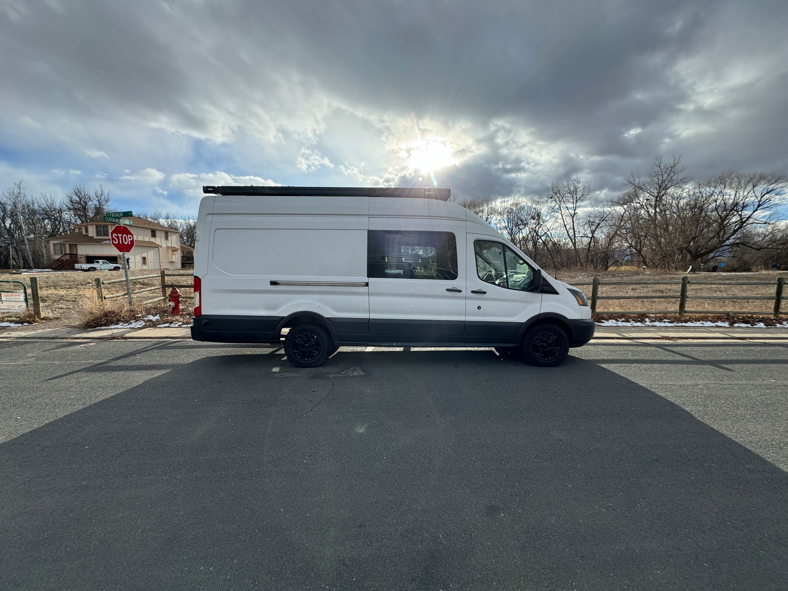 White camper van, resembling an RV rental, parked on a road under a sunlit, cloudy sky.