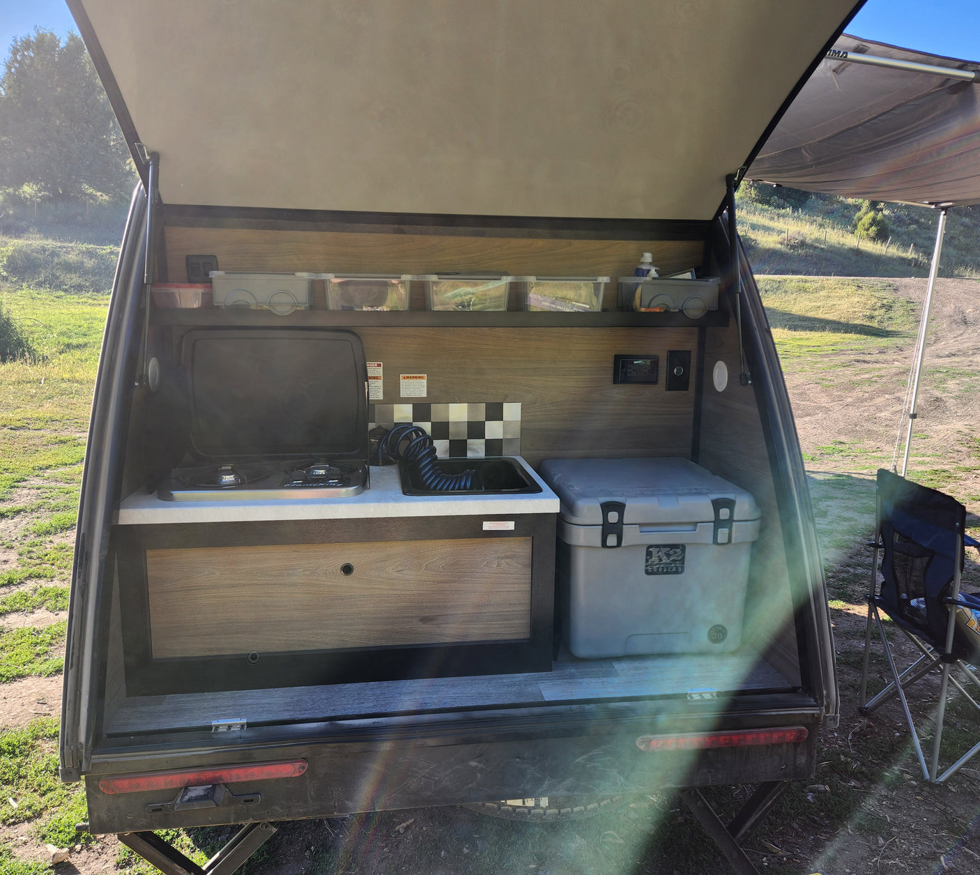 RV rental teardrop camper outdoor kitchen. View inside the rear hatch with stove, sink, cooler, and storage. Perfect for camping.