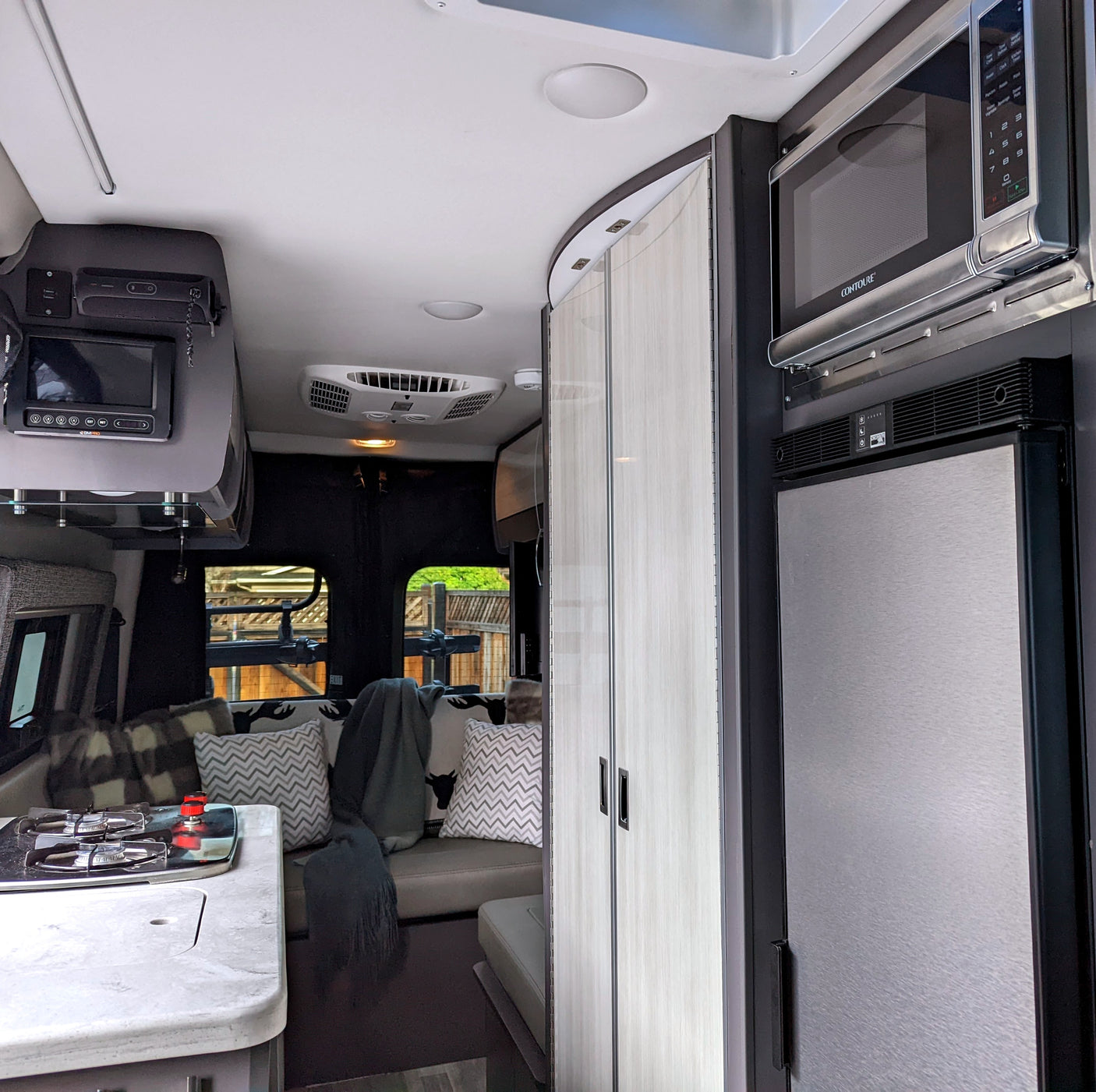 Bright, modern rv rental interior showcasing a compact kitchen with stove, cozy seating area, overhead control panel, microwave, and fridge.