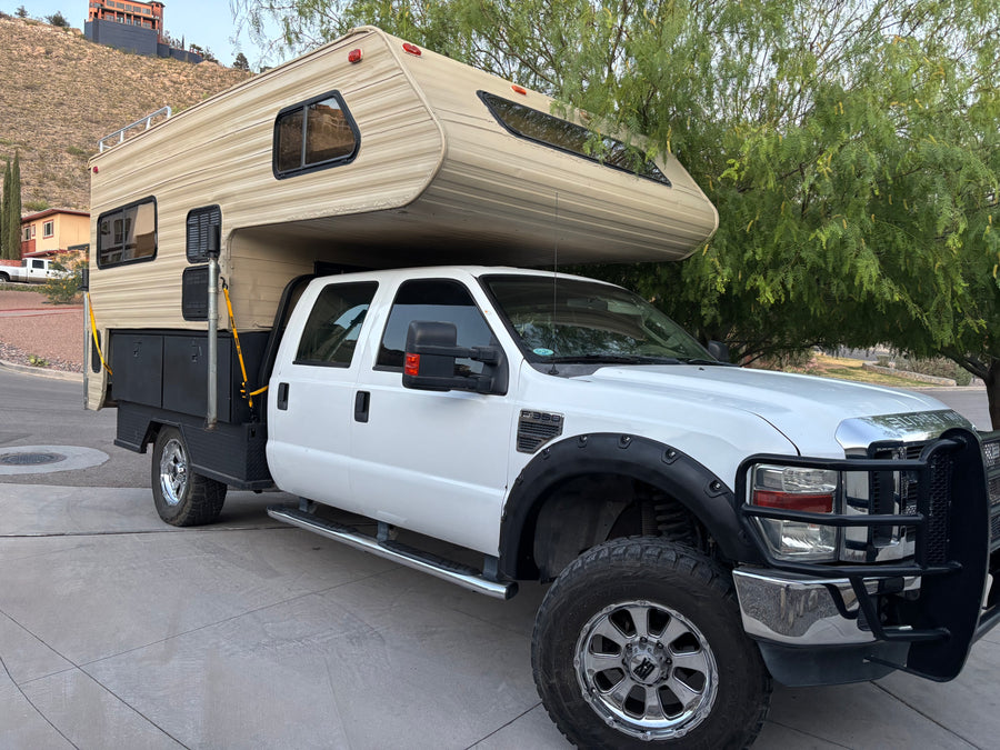 This white Ford F-350 pickup truck fitted with a large, beige truck camper is ready for an rv rental adventure.