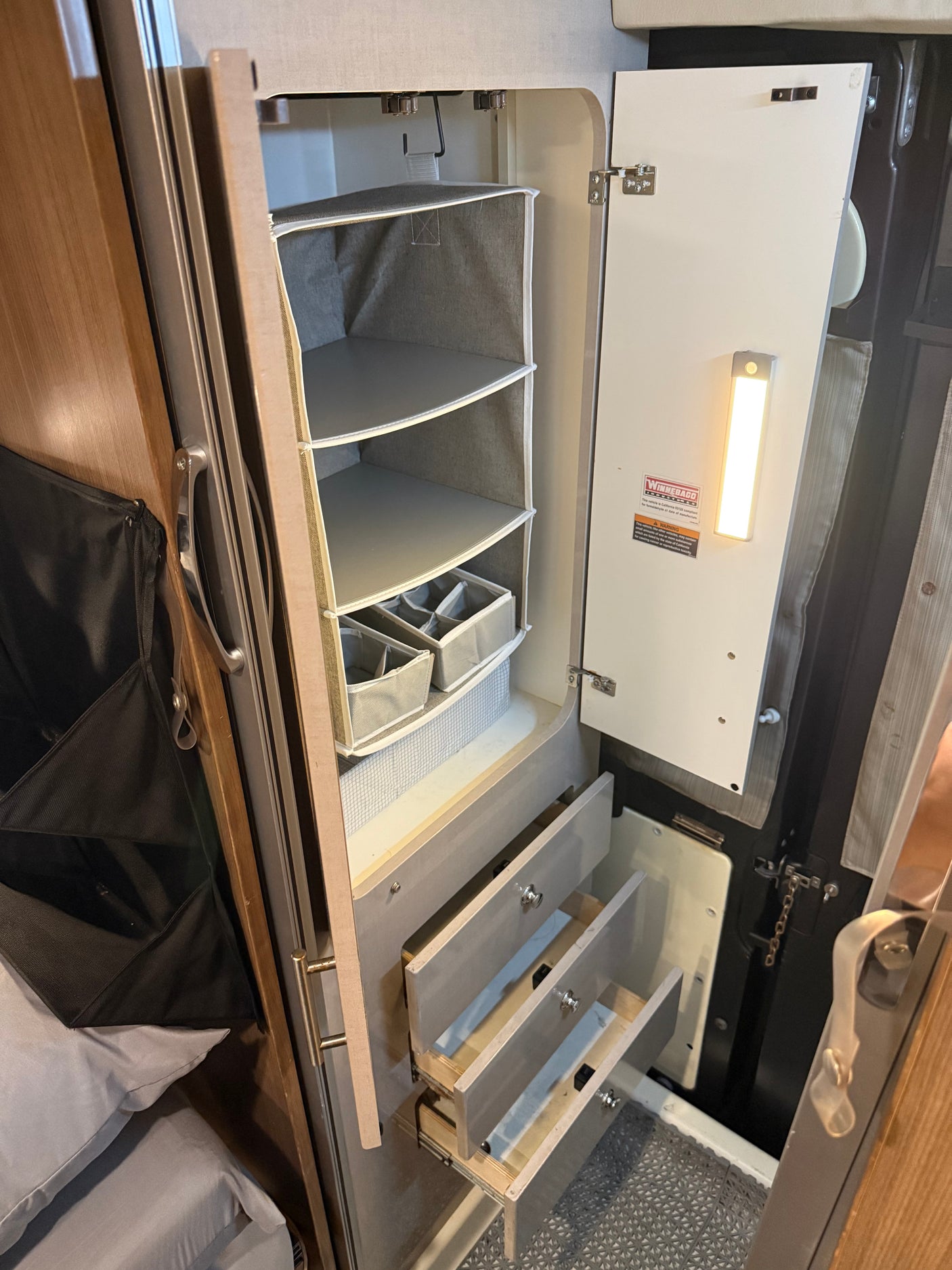 Organized RV rental closet featuring hanging storage, pull-out drawers, and an LED light for efficient space use.