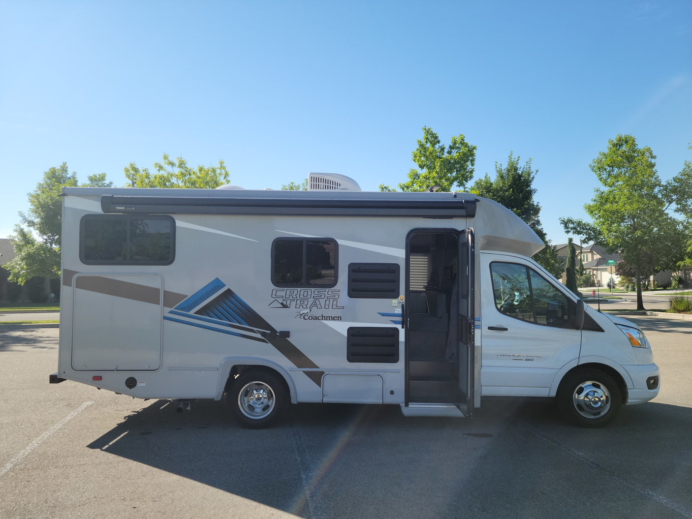 This white and gray Coachmen Cross Trail motorhome rv rental, parked on a sunny day with its door open.