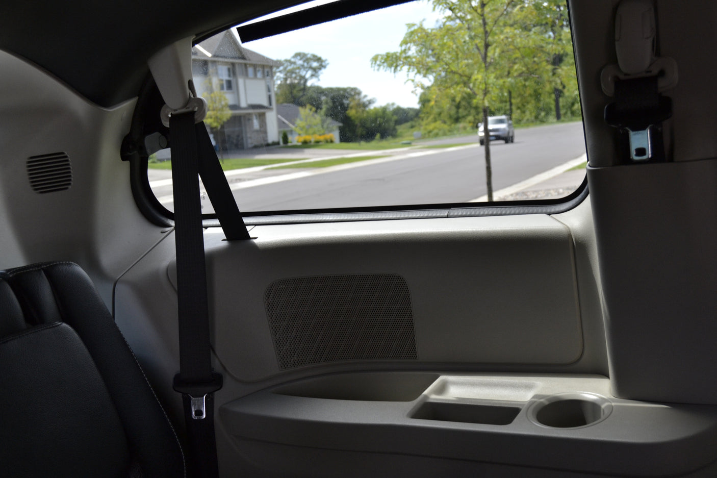 Inside a bright RV rental: passenger seat, side panel with speaker, and a clear view of a suburban road.