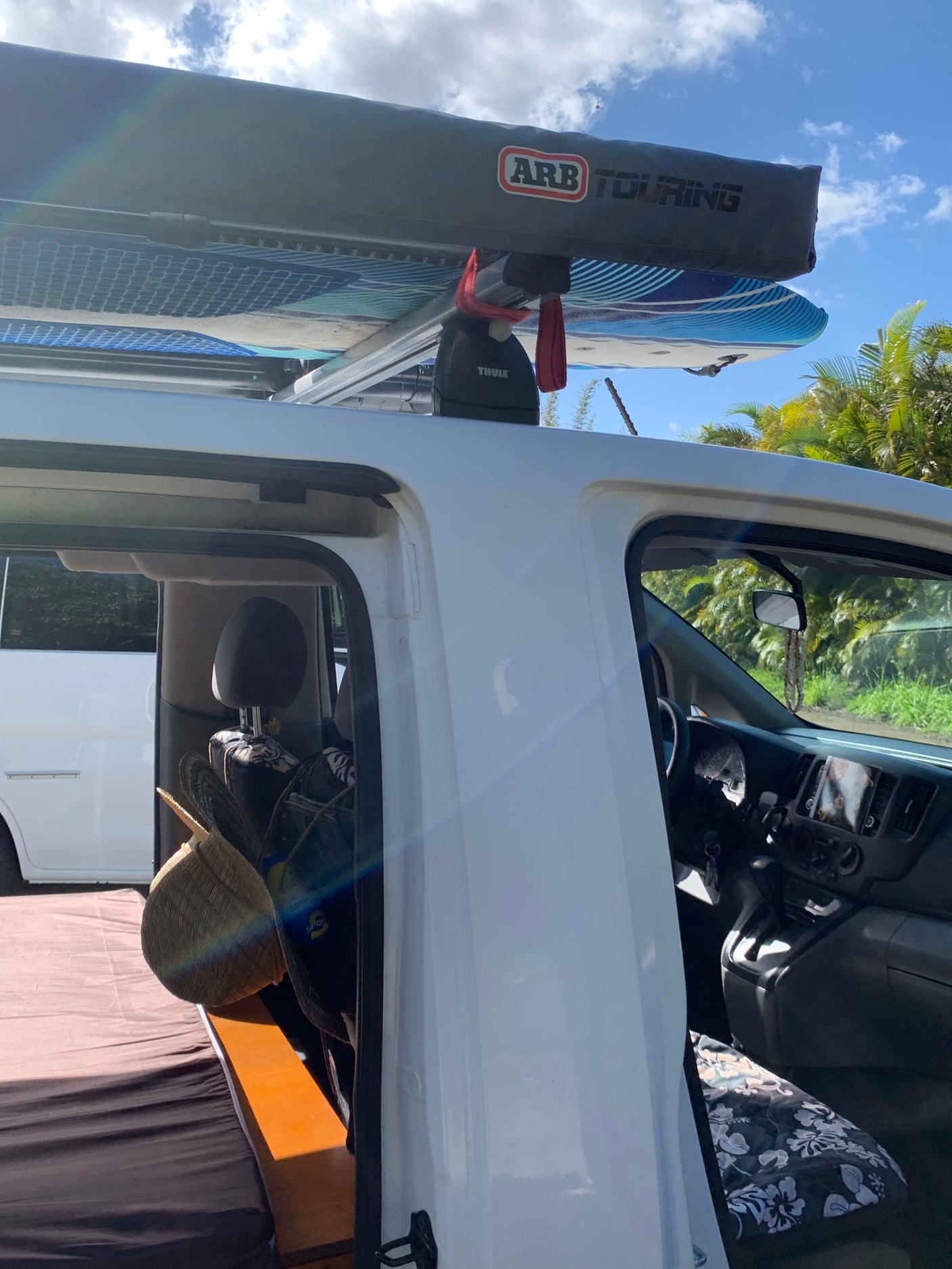 An RV rental set up for van life, featuring surfboards and an ARB awning on the roof. Its open door reveals a cozy bed inside.