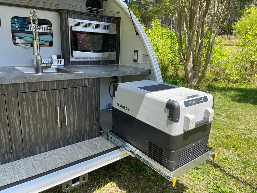 sits ready on green grass.|White & blue teardrop travel trailer for rv rental. Luna camper parked on grass