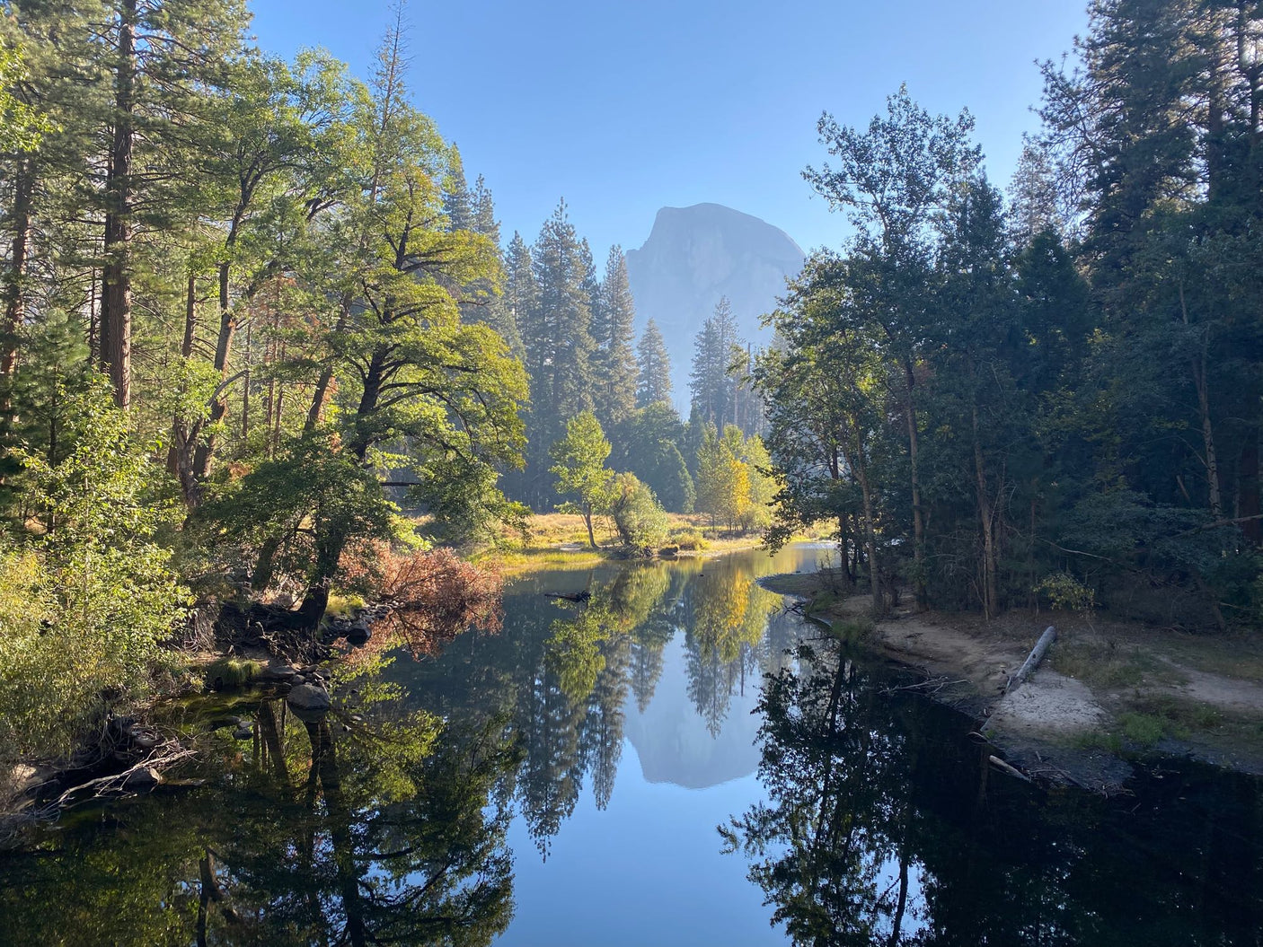 Scenic Yosemite view: A tranquil river mirrors lush trees and Half Dome. Ideal for your next rv rental adventure.