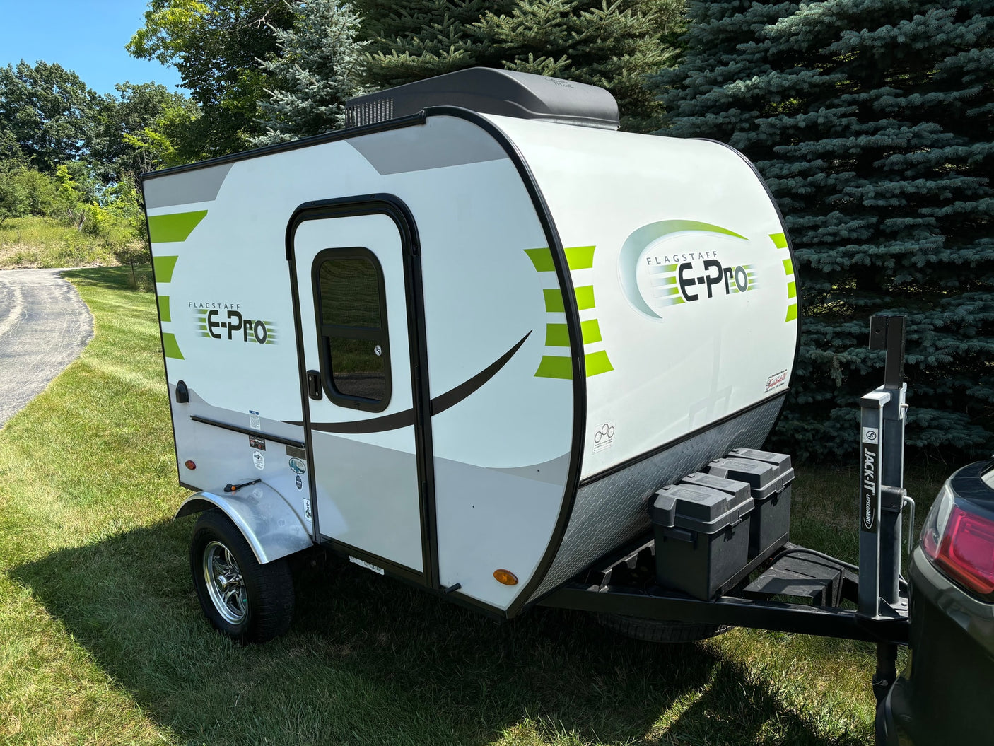 A white and green Flagstaff E-Pro travel trailer, perfect for an RV rental, parked on sunny grass with trees behind it.