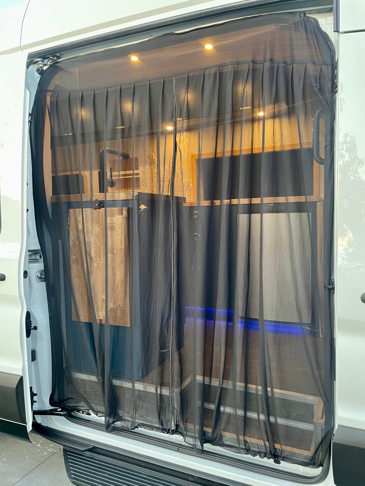 Interior view of an RV rental camper van with a closed magnetic mesh screen door, revealing a functional kitchen and warm lighting.