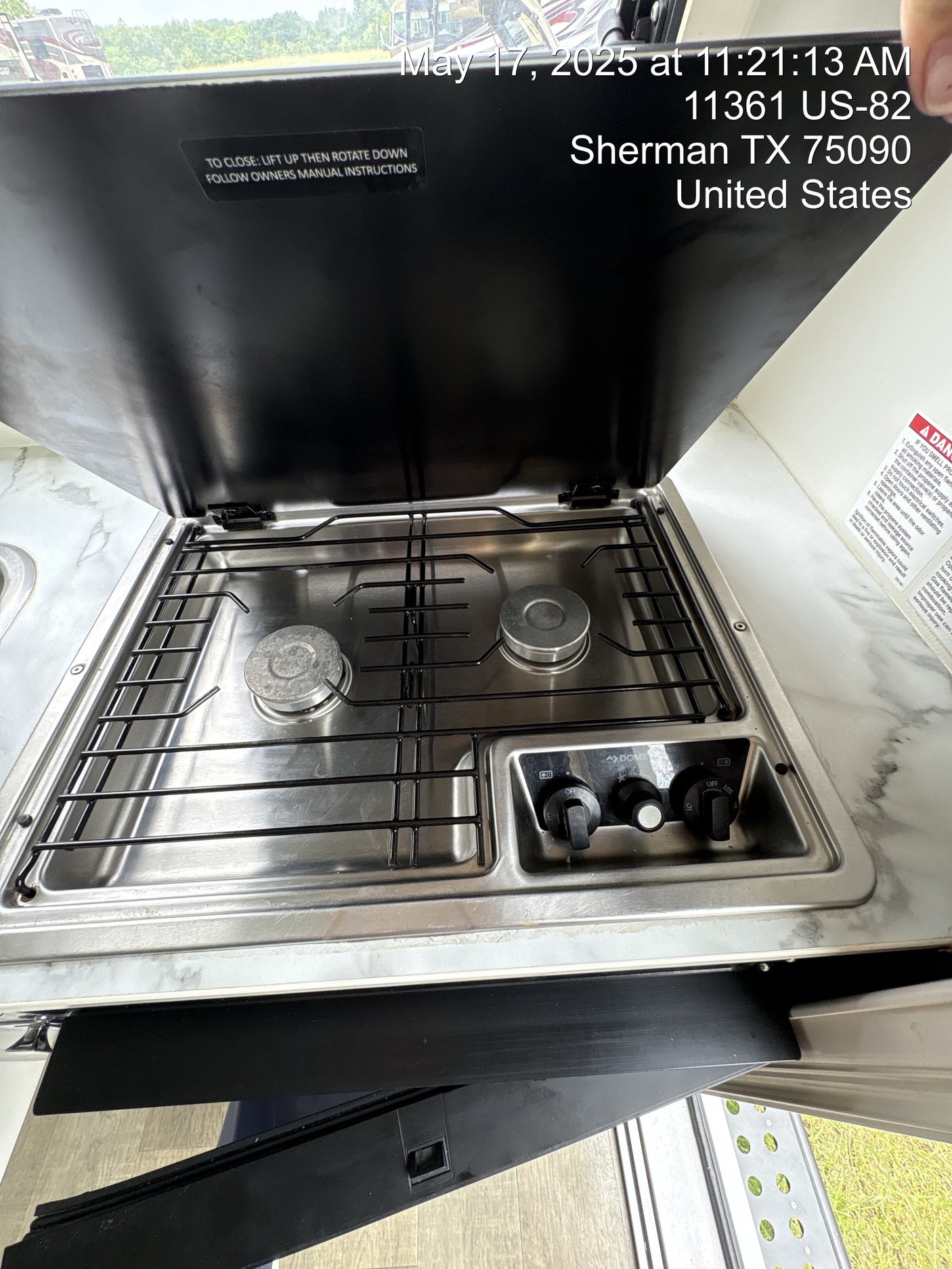 RV rental: An open stainless steel two-burner propane cooktop with grates and control knobs. Safety warnings visible.