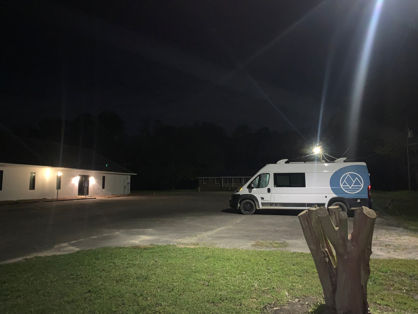 White "Essentials" RV rental van parked in a lit lot at night next to a white building.