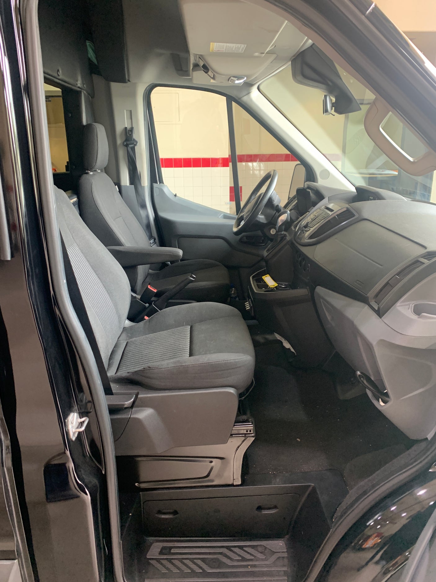 Interior view of a black RV rental van's front cabin, showing grey driver and passenger seats, dashboard, and steering wheel.