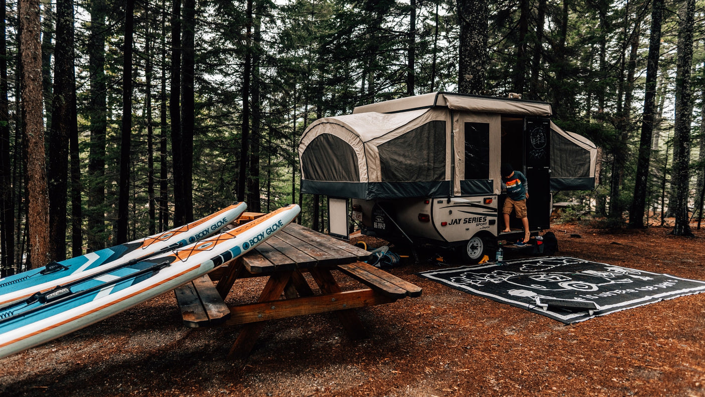 Enjoying nature with an RV rental: a campsite setup featuring a pop-up camper, paddleboards, and a picnic table.