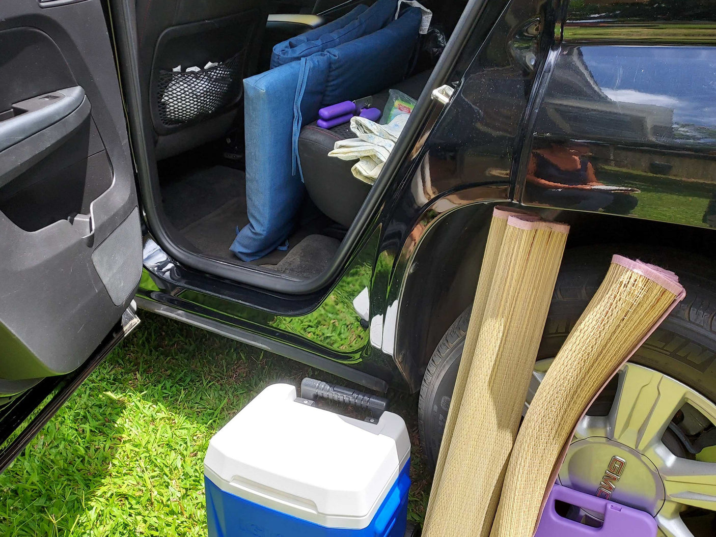 Car packing for RV rental trip: blue cushions, cooler, and rolled mats.