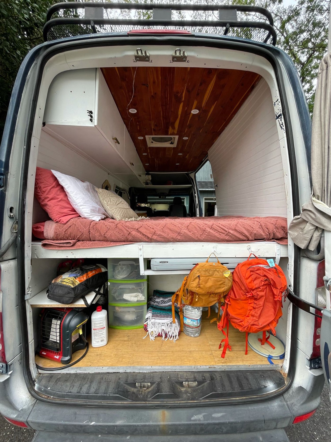 RV rental van interior: A cozy bed with pink bedding, pillows, and organized storage for mobile living and travel. — photo 5