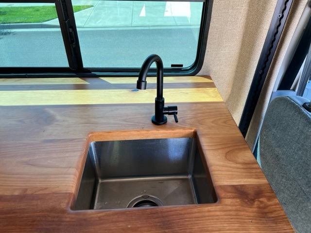 Modern rv rental interior featuring a wood countertop, sleek sink, and black faucet. Perfect for road trips!
