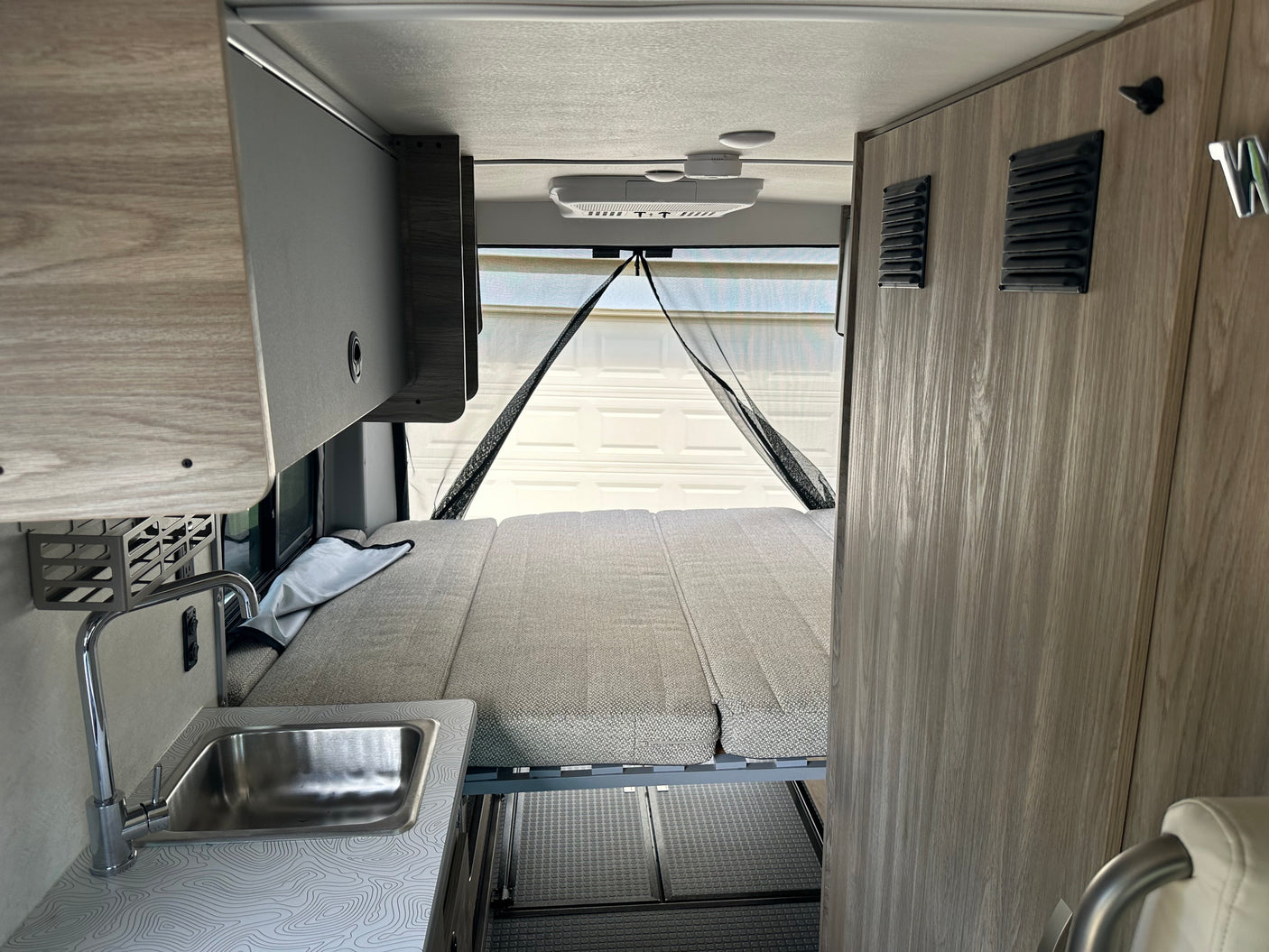 RV rental interior featuring a convertible bed, compact kitchen with sink, and overhead storage. Ideal for travel.