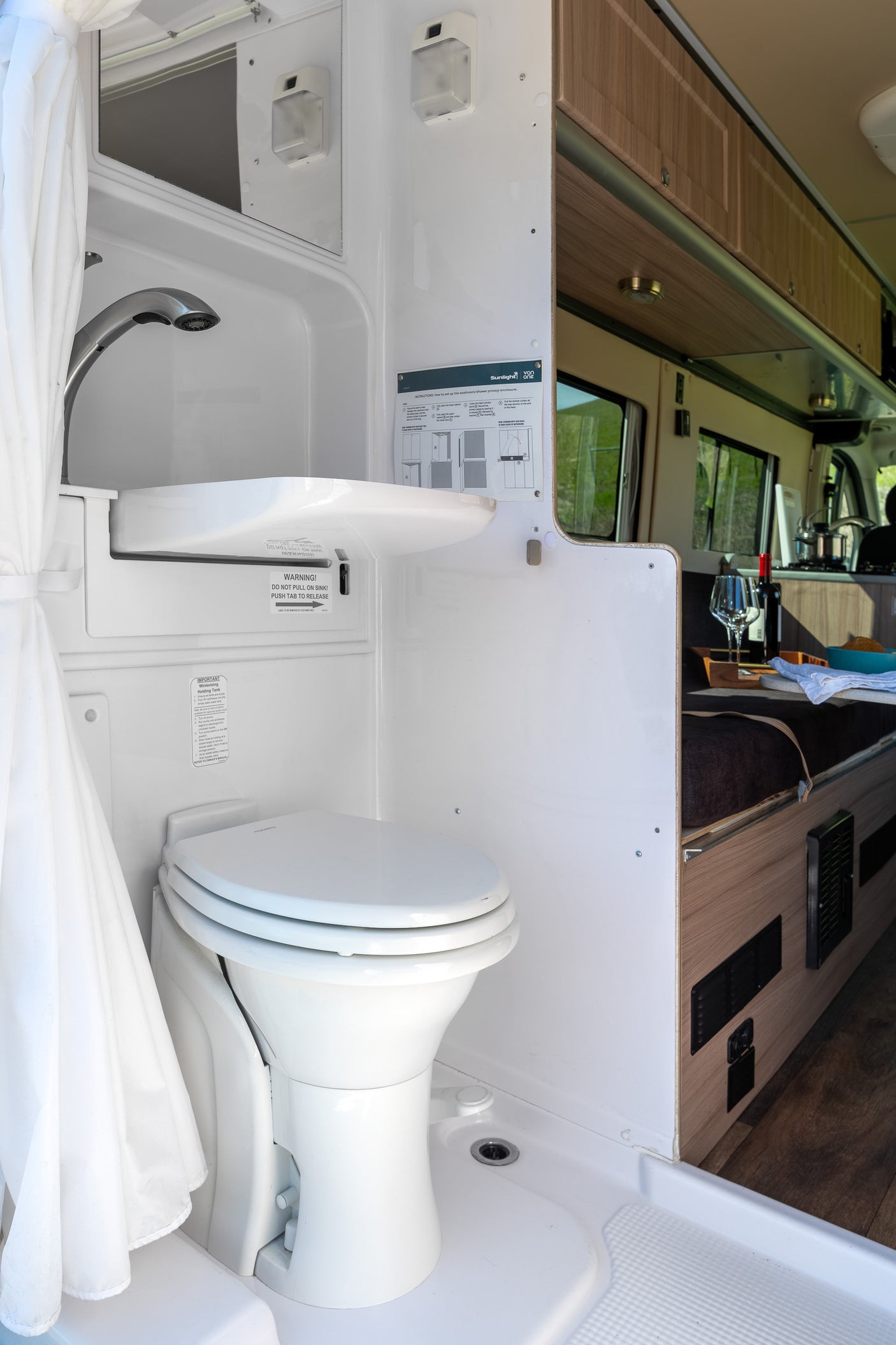 Efficient RV rental bathroom featuring a toilet, integrated pull-out sink/shower, and privacy curtain. Perfect for camper van travel.