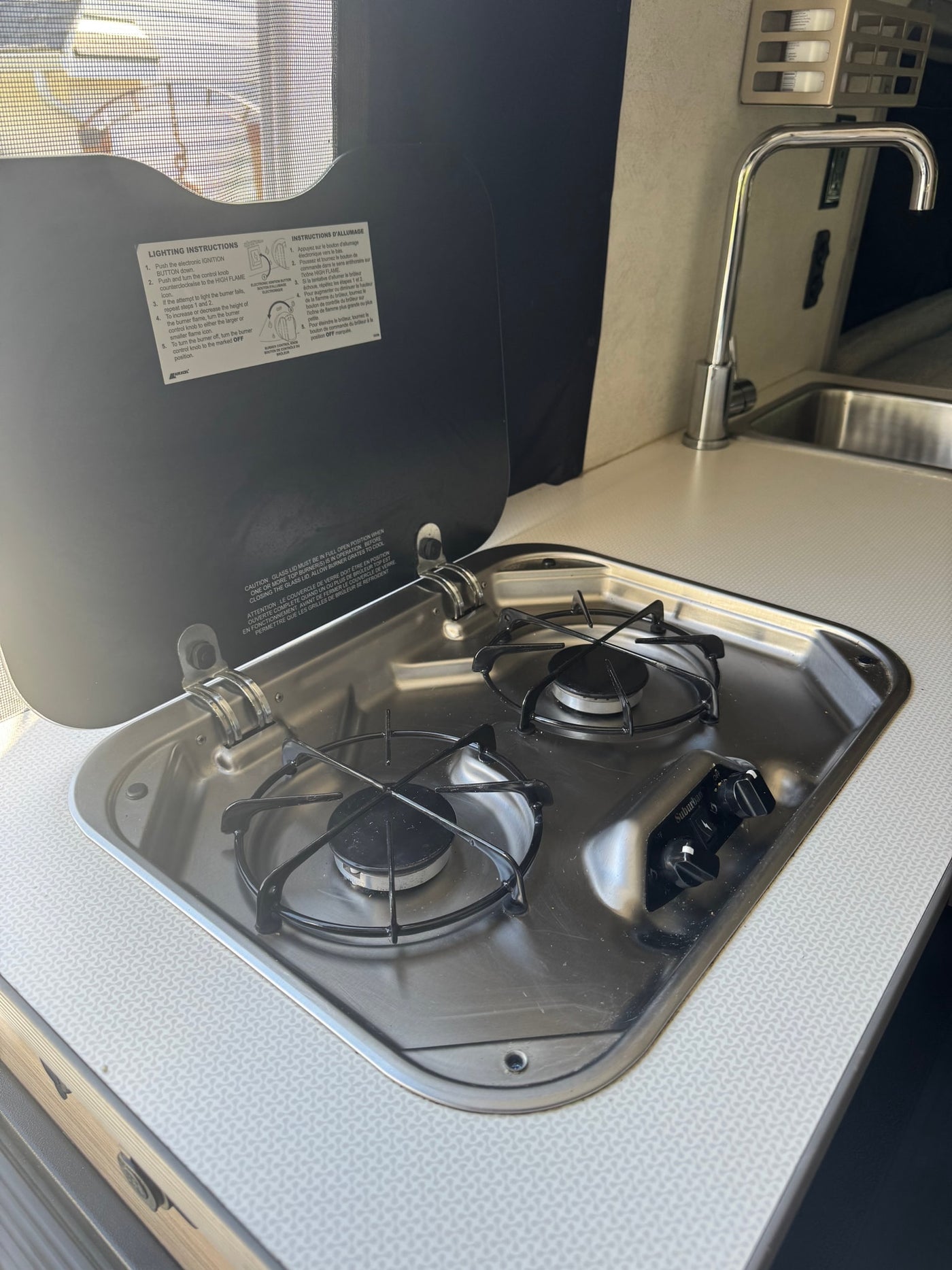An RV rental kitchen with an open lid, revealing a two-burner gas stove, sink, and operating instructions. — photo 7
