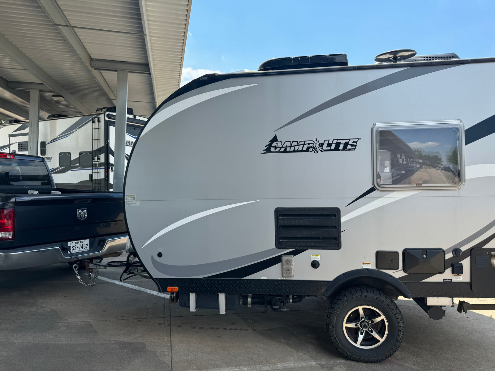 Grey CampLite travel trailer, perfect for RV rental, hitched to a pickup truck under a shelter, ready for camping.