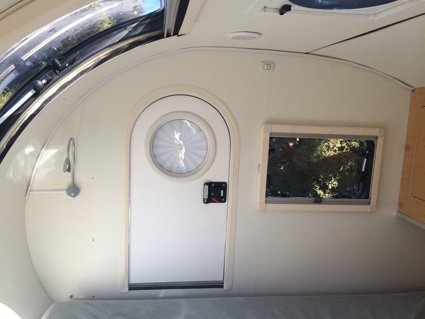 View inside an RV rental: large overhead skylight, a round entry door, and a rectangular side window to nature.