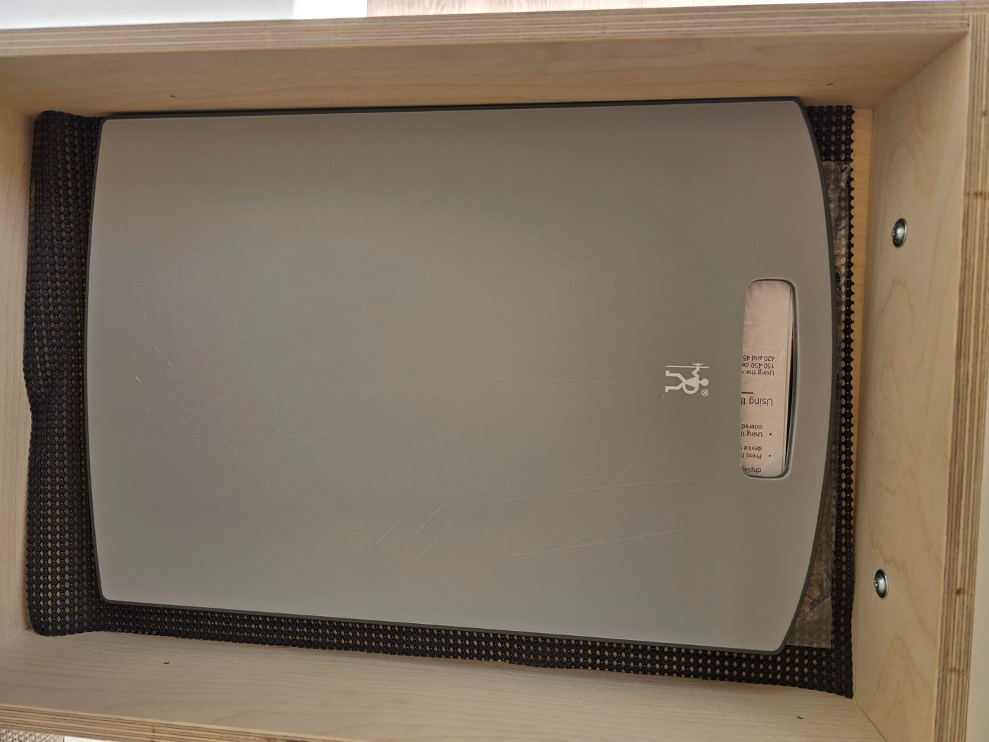 RV rental: Gray cutting board with a logo, on a black non-slip mat within a light wood storage cabinet.