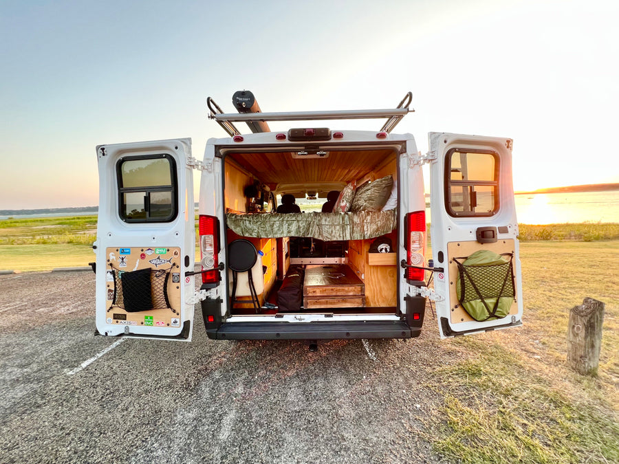 RV rental for adventure! Open doors show a custom camper interior, rooftop Road Shower, and sunset over the lake.