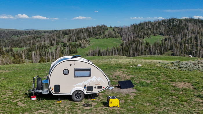 An rv rental teardrop camper (Boondock model) is set up for off-grid adventure with solar panels & generator in a scenic landscape.