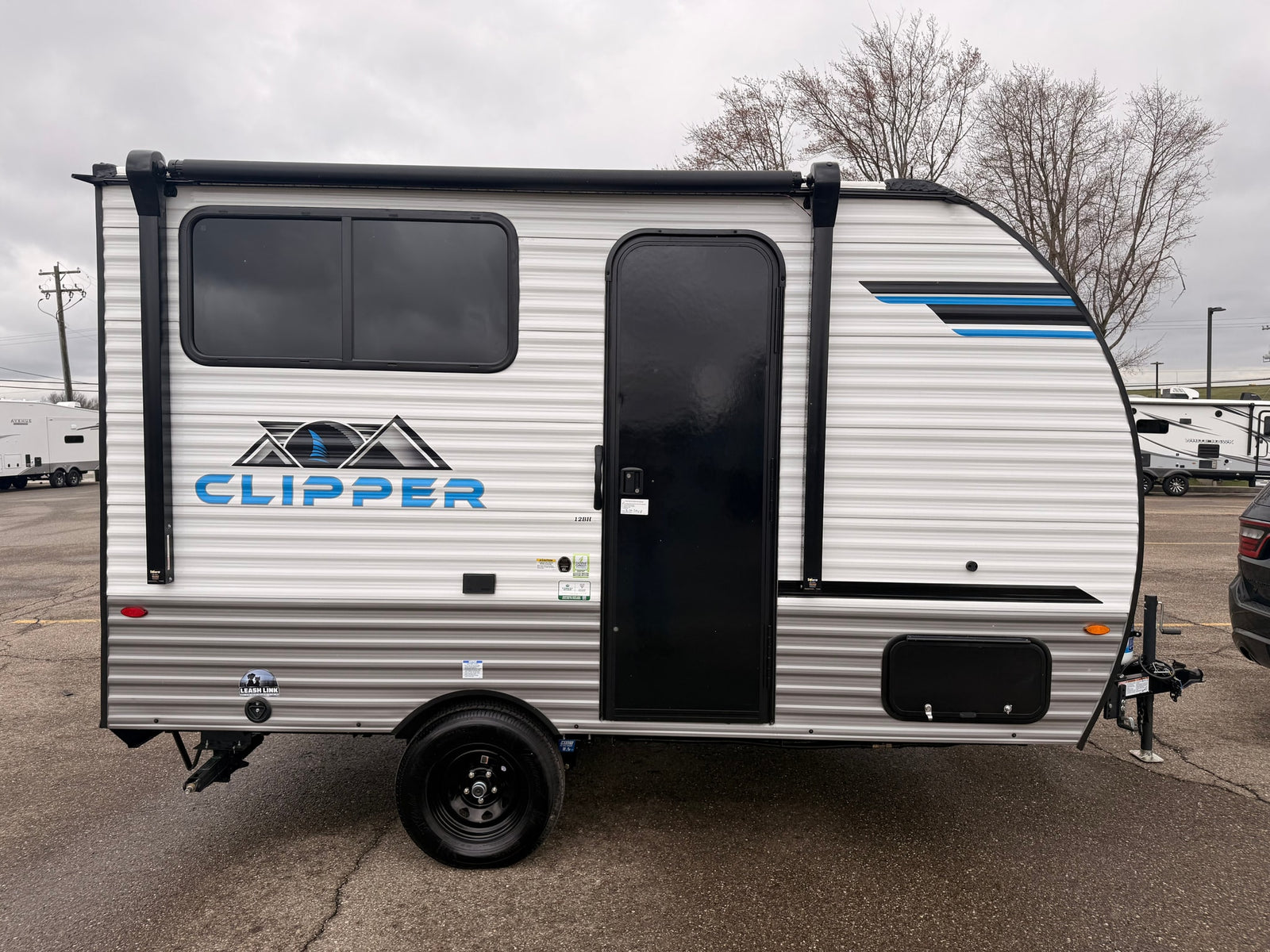 A white Clipper travel trailer, an ideal rv rental unit, parked on a gray day. Features black windows, door, and awning.
