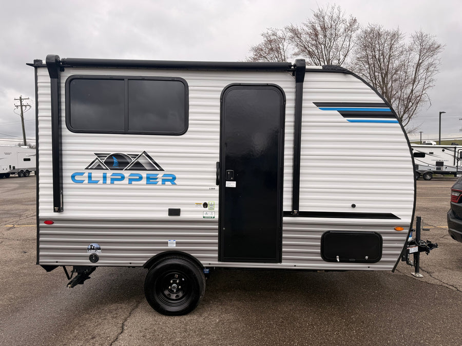 A white Clipper travel trailer, an ideal rv rental unit, parked on a gray day. Features black windows, door, and awning.