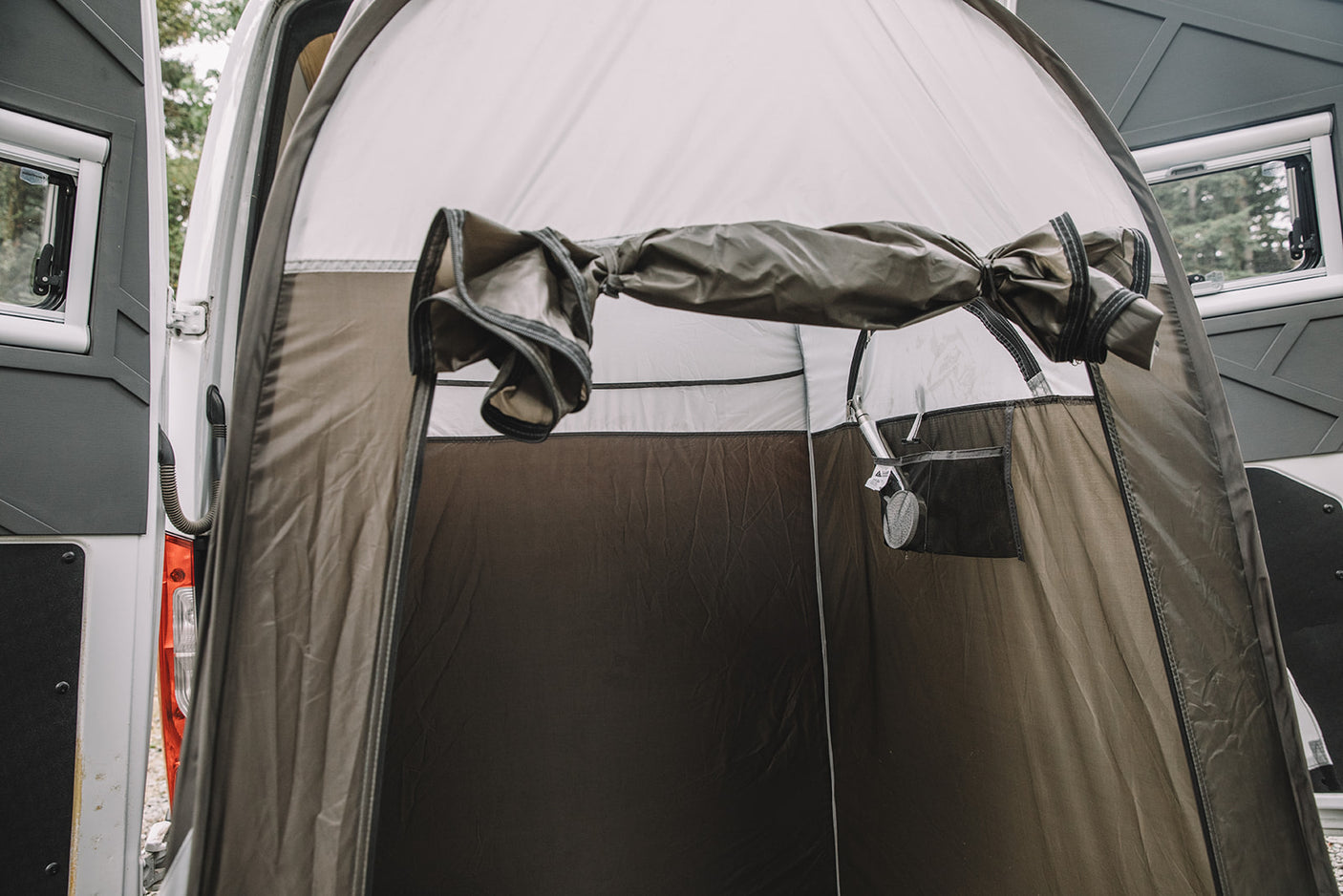 RV rental camper van's outdoor privacy shower tent, shown attached to the rear. The brown tent interior has a visible shower head.