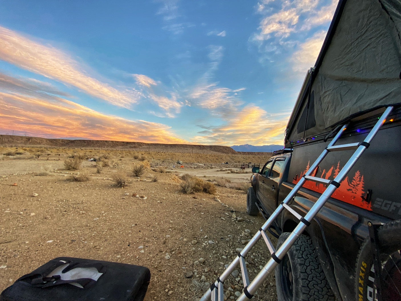 RV rental adventure: Truck with rooftop tent enjoying a vibrant desert sunset.