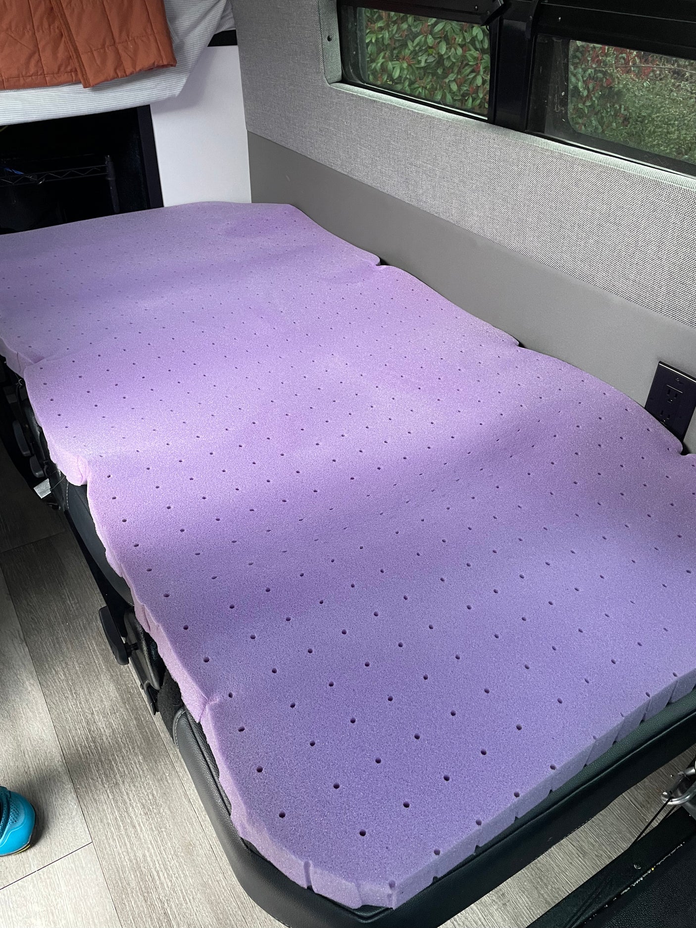 Enhancing comfort in your RV rental: a purple, perforated foam mattress topper on the bed, with an outlet nearby.