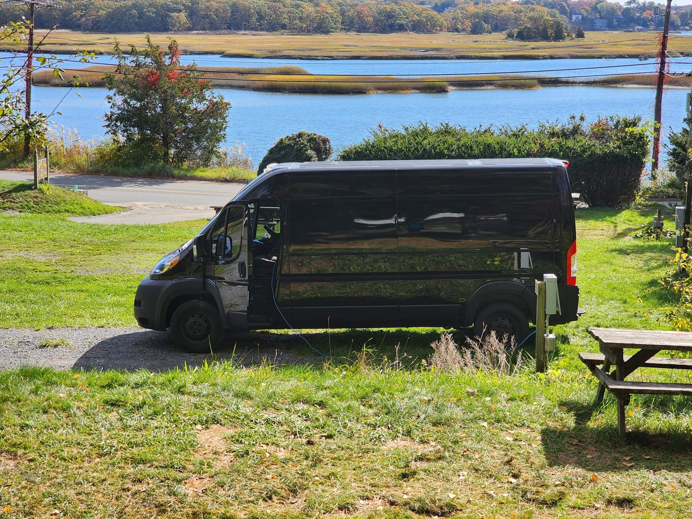 connected to power. A scenic stop for van life camping and outdoor adventure.|Black RV rental van at a damp campsite with picnic tables