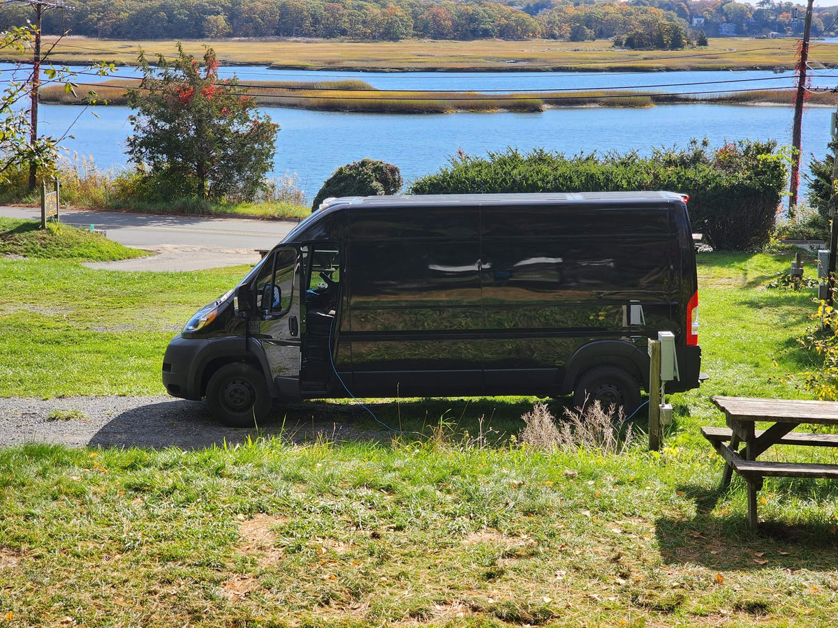 connected to power. A scenic stop for van life camping and outdoor adventure.|Black RV rental van at a damp campsite with picnic tables — photo 3