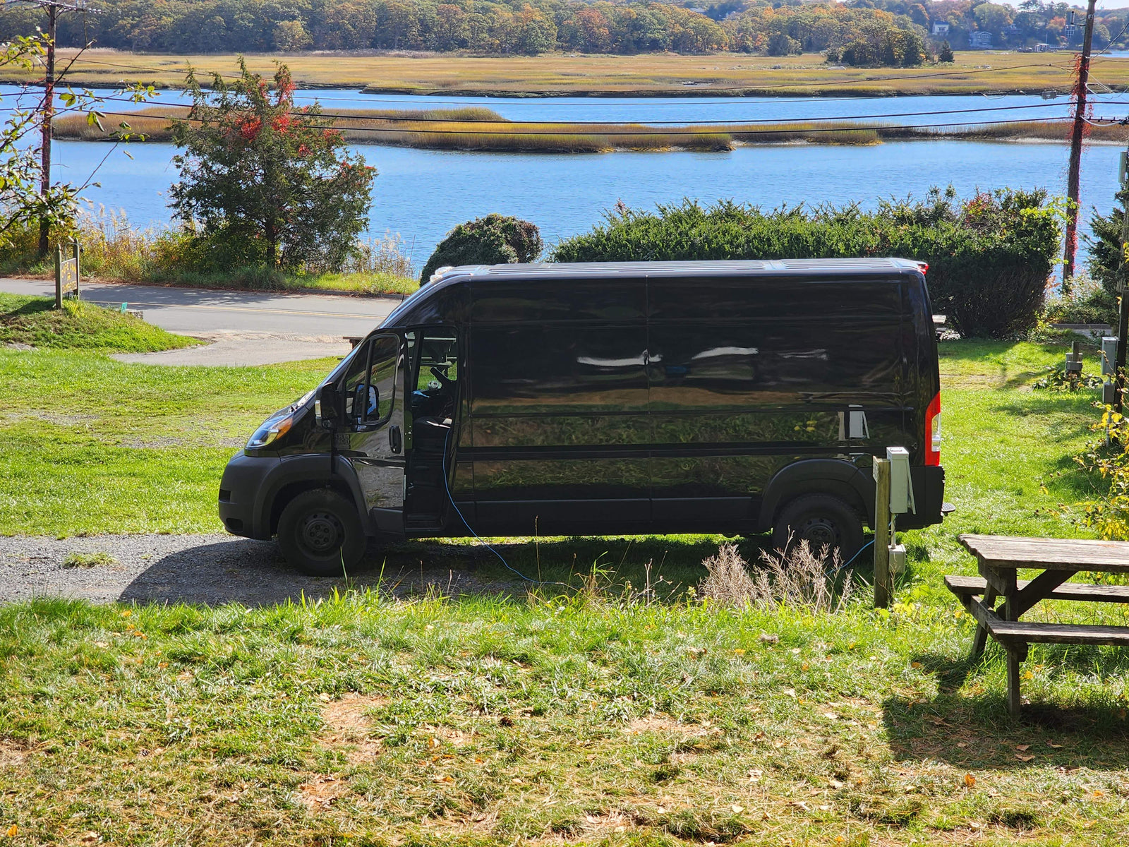 Black RV rental van parked by a serene marsh, connected to power. A scenic stop for van life camping and outdoor adventure.